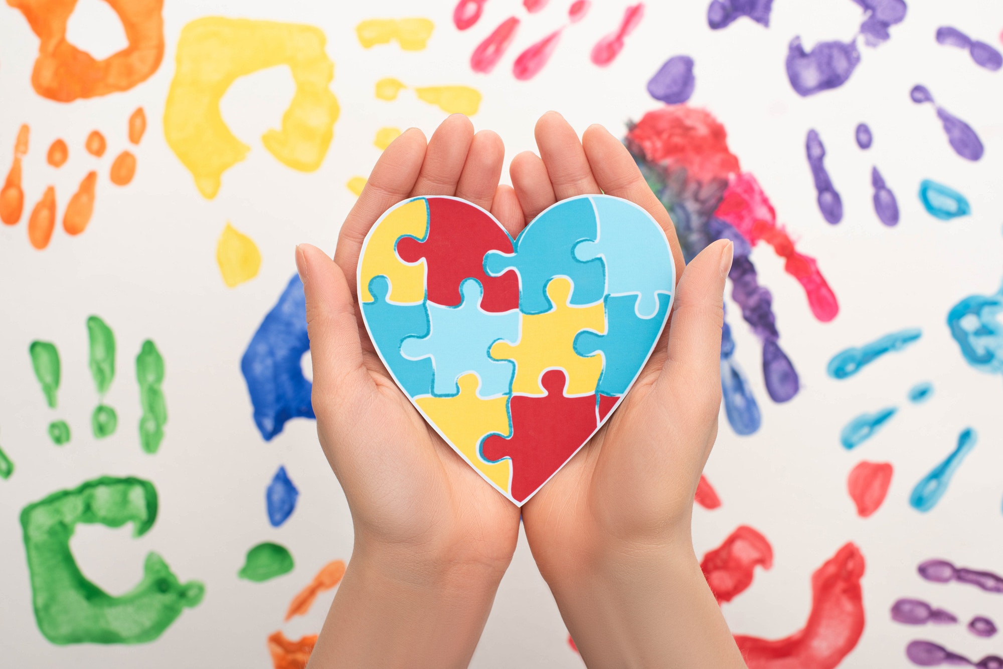 cropped view of woman holding heart with puzzle on white with hand prints for World Autism Awareness