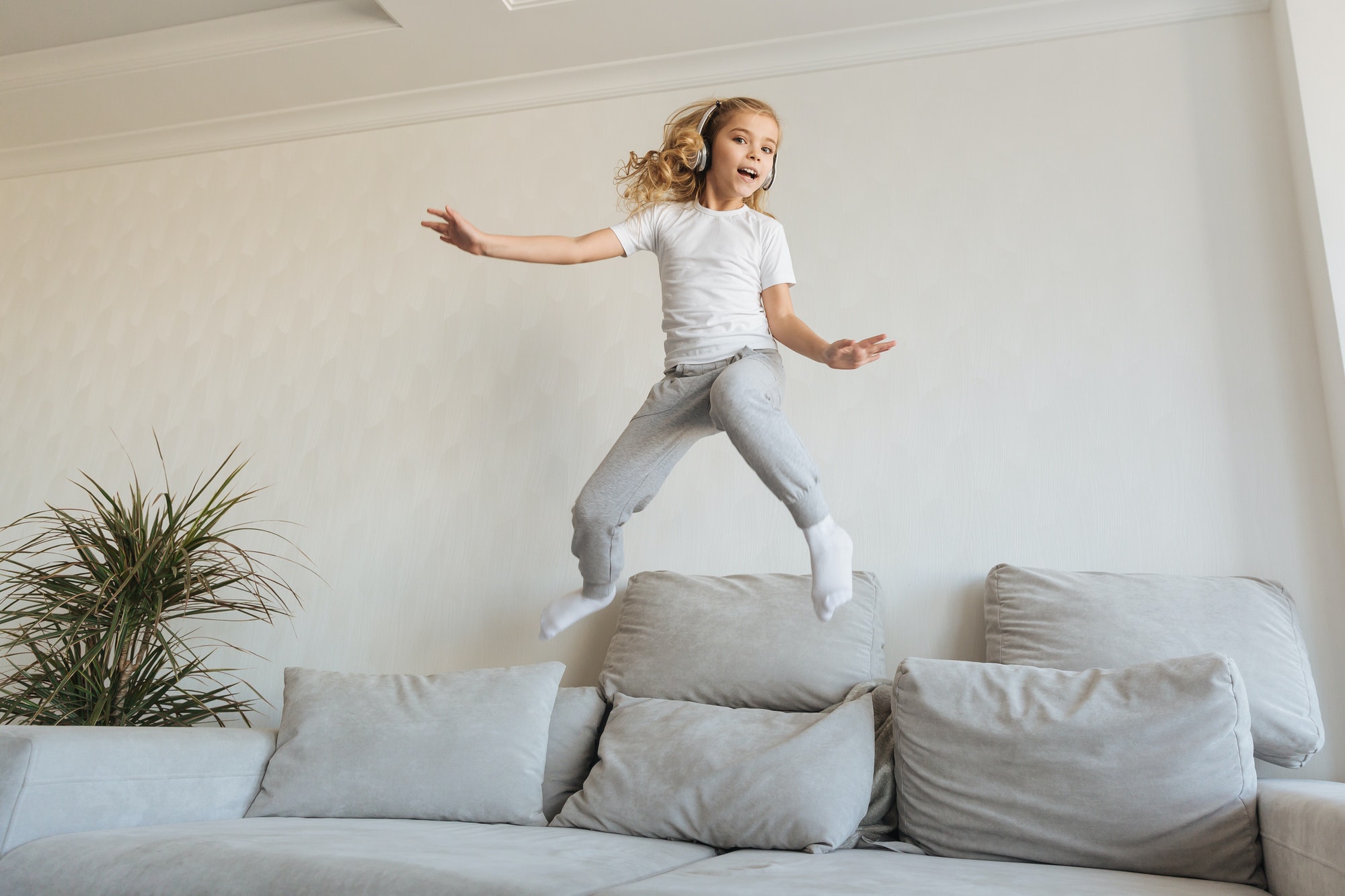 smiling kid jumping on sofa and listening music with headphones