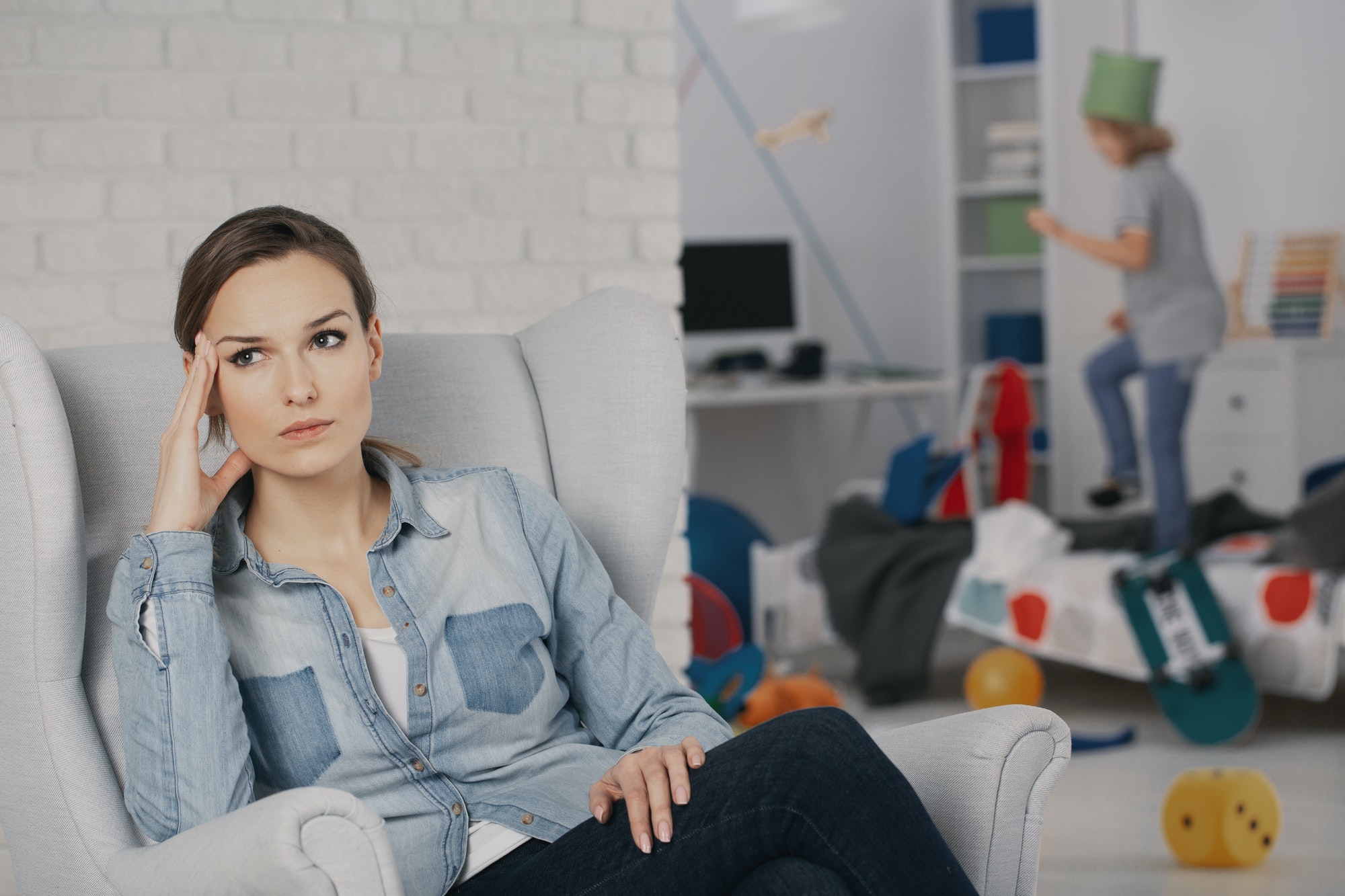 Worried mother relaxing on armchair while son with adhd making a